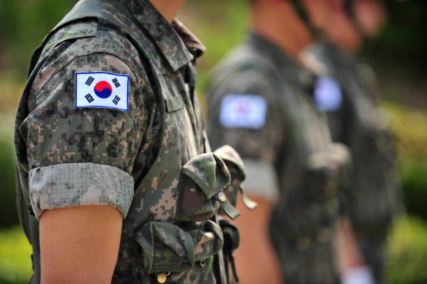 대한민국 군복을 착용한 남성 군인들이 야외에서 일렬로 정렬해 서 있는 모습. 팔에는 태극기 패치가 부착되어 있다.